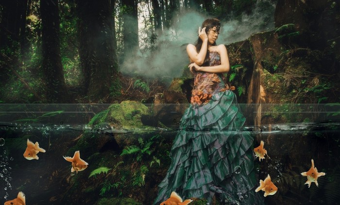 Woman in fantasy dress with goldfish in forest pond