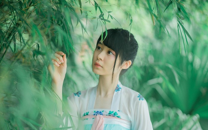Young Asian woman in traditional dress among bamboo leaves