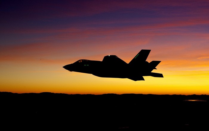 Silhouette of F-35 fighter jet against a sunset sky