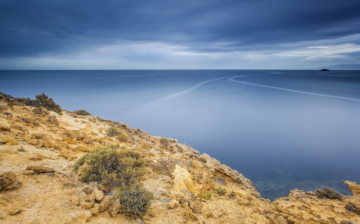 Rocky coastline overlooking a calm sea under cloudy sky