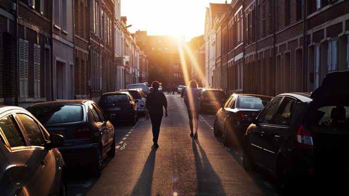Two people walk down a street at sunset