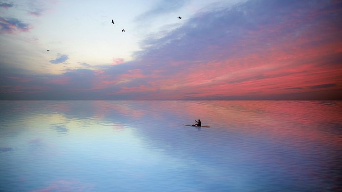 Person on paddleboard at sunset over the ocean