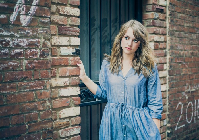 Woman in blue dress leaning against brick wall