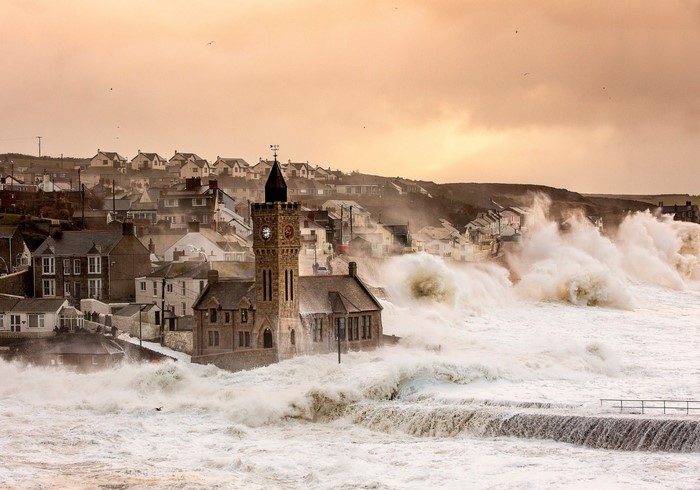 Stormy waves crash against a coastal town with a clock tower