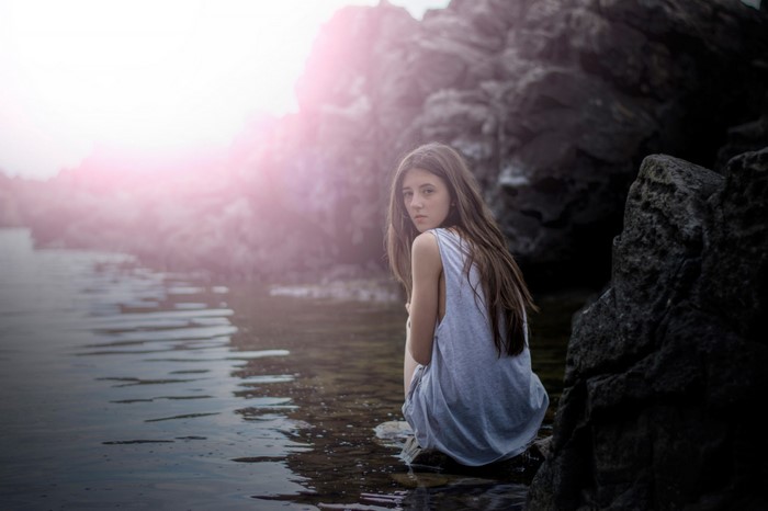 Young woman sitting by the water on rocks