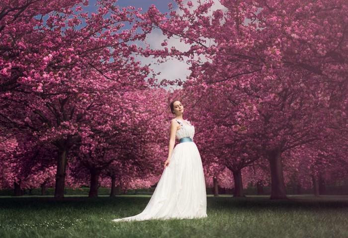 Woman in white gown standing among cherry blossom trees