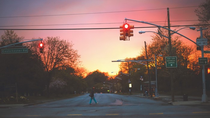 Person crossing street at sunset with traffic lights