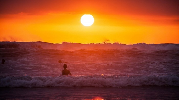 Sunset over the ocean with people swimming