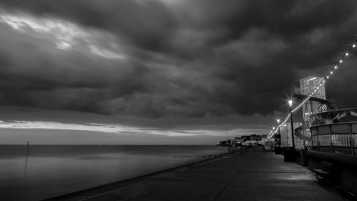 Monochrome seascape with pier lights and stormy clouds