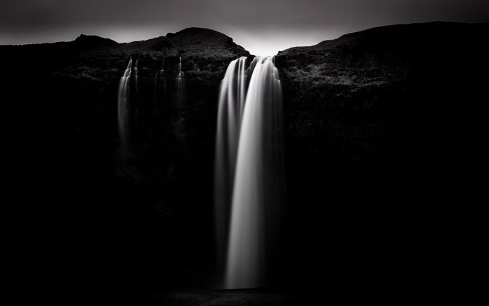 Monochrome waterfall cascading down a dark cliff