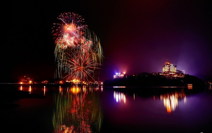Fireworks over a lake at night with a building reflection