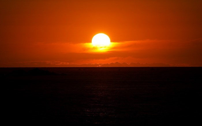 Sunset over the ocean with a bright sun on the horizon