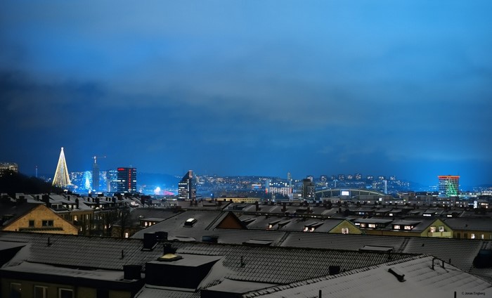 Cityscape at night with snow-covered rooftops and illuminated buildings