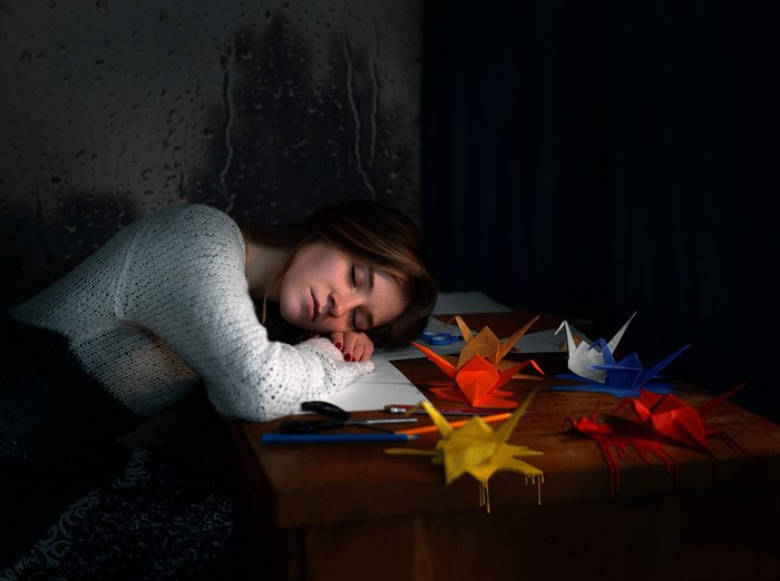 Woman sleeping at a desk with origami cranes