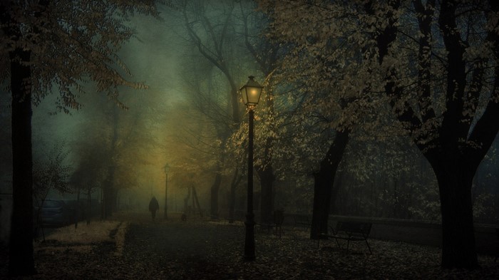 A foggy park at night with a lamppost and a person walking