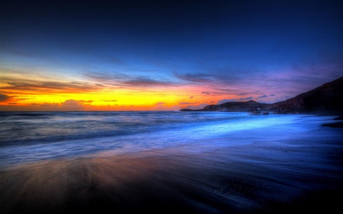 Sunset over a beach with waves and mountains