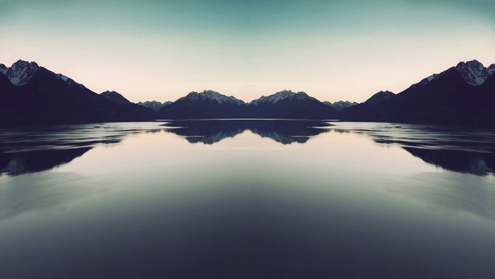 Symmetrical mountain range reflected in a calm lake at dawn