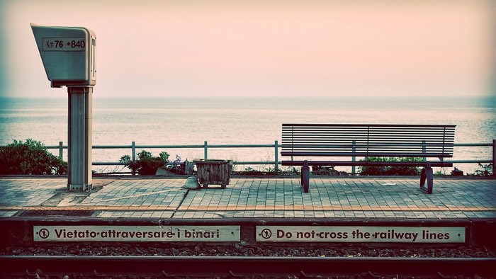 Train station platform by the sea with a bench and sign