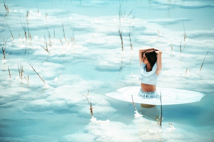 Woman in white dress standing in shallow blue water with dry reeds