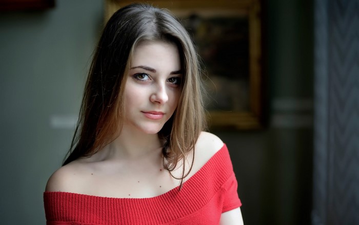 Woman with long brown hair wearing a red off-the-shoulder top