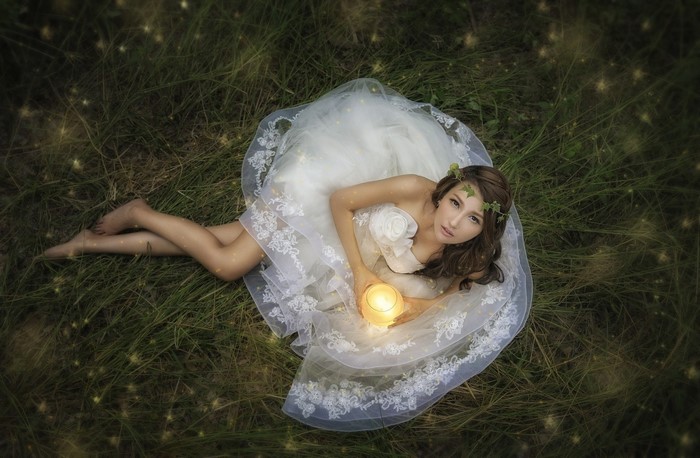 Woman in white dress holding a candle in grass