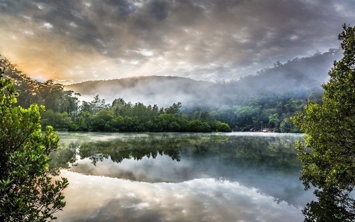 Misty morning over a calm lake with forested hills