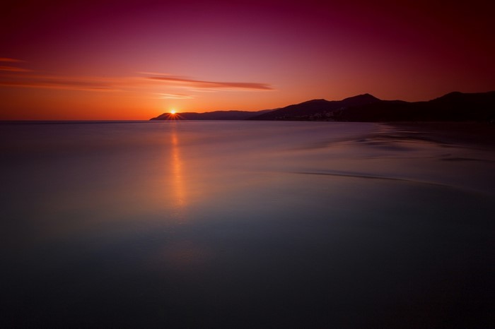 Sunset over the ocean with mountains on the horizon