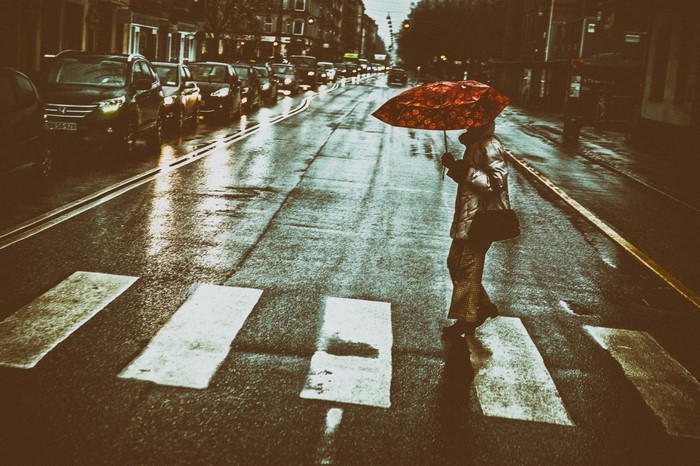 Person with umbrella crossing street in rain