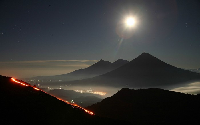 Volcano eruption at night with moon and mountains