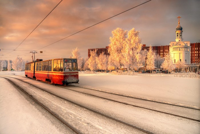 Red tram on snowy tracks in front of a church at sunrise