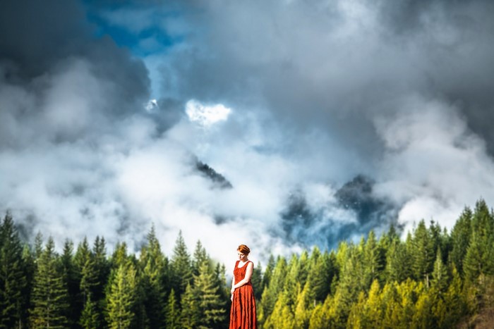 Woman in red dress in front of cloudy mountains and forest