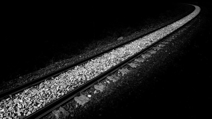 Monochrome image of train tracks curving into darkness
