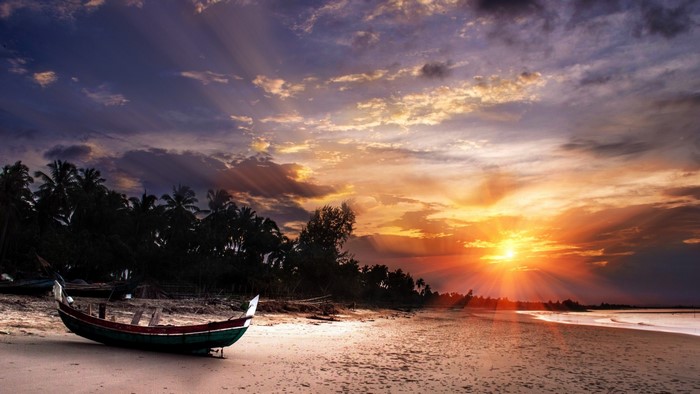Boat on a beach at sunset with palm trees