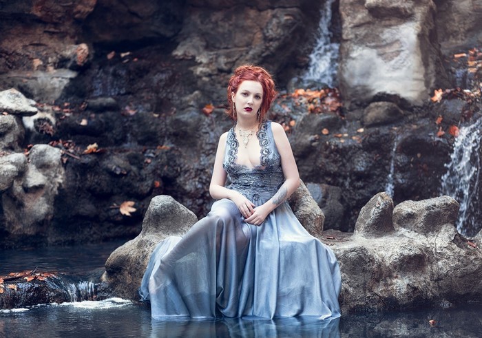Woman in a flowing dress sitting by a waterfall