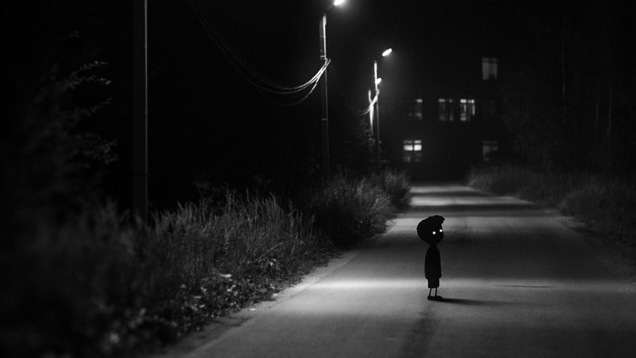 Boy with glowing eyes on a dark road at night