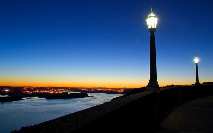Street lights overlook a city and river at dusk