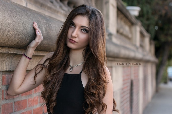Woman with long brown hair posing by a brick wall