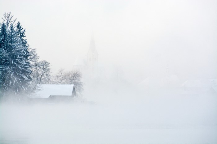 Winter landscape with snow-covered house and church in fog