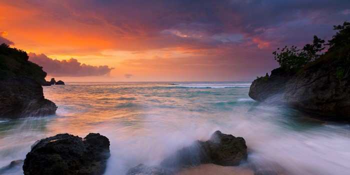 Sunset over the ocean with waves crashing on rocks