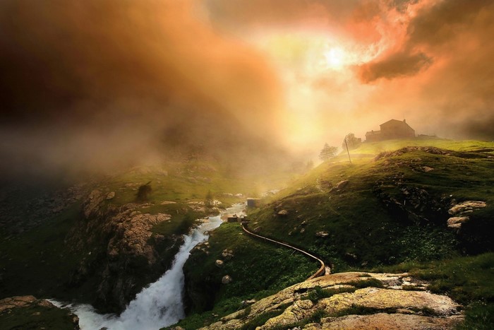 Misty mountain landscape with a house and river at sunrise