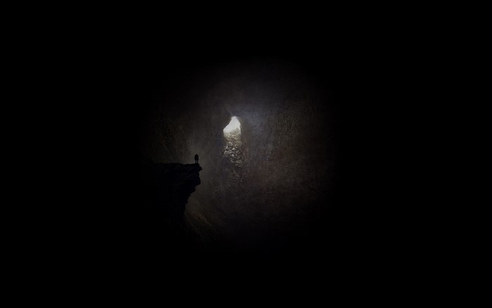 Person standing on cliff edge in dark cave with light opening