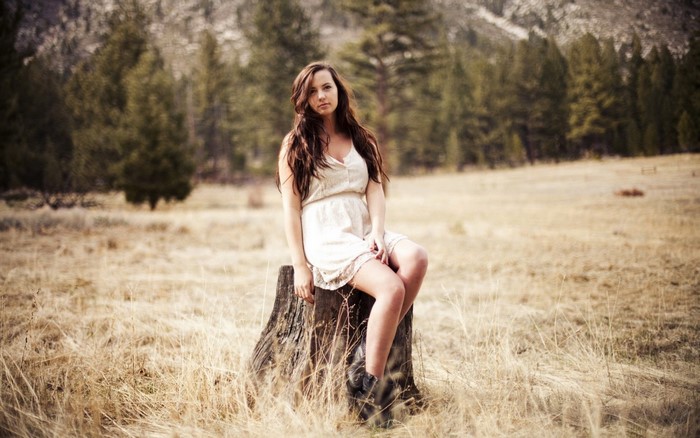 Woman sitting on a tree stump in a field