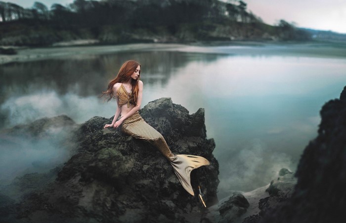 Mermaid sitting on rocks by the water