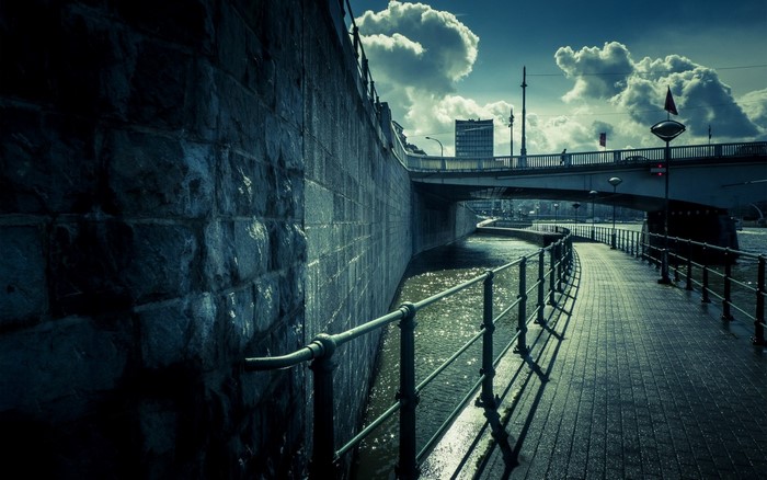 Stone wall and walkway along a river under a bridge