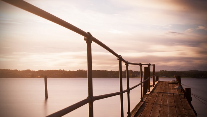 Wooden pier with railing over calm water at sunset