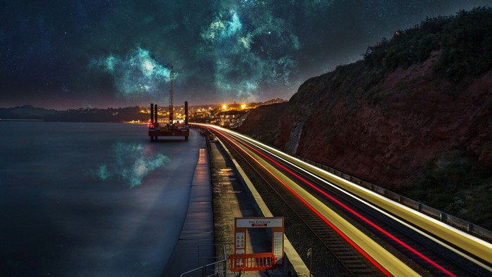 Train tracks and oil rig at night with nebula sky