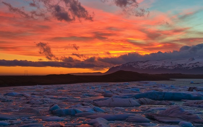 Icebergs floating in a lake at sunset with mountains