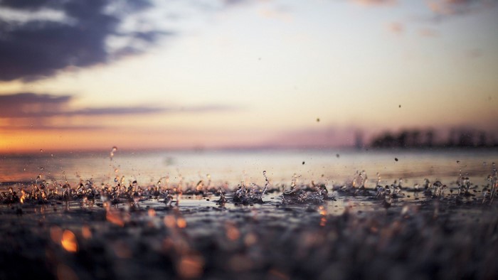 Raindrops splashing on water at sunset