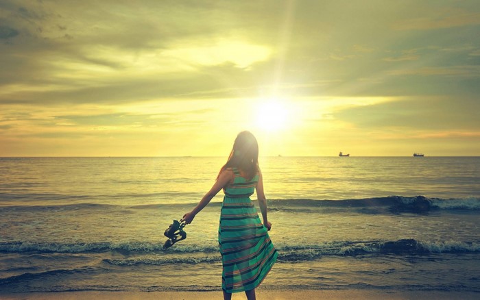 Woman holding shoes on a beach at sunset