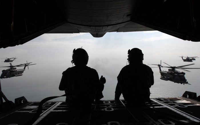 Silhouettes of soldiers in a military aircraft with helicopters flying